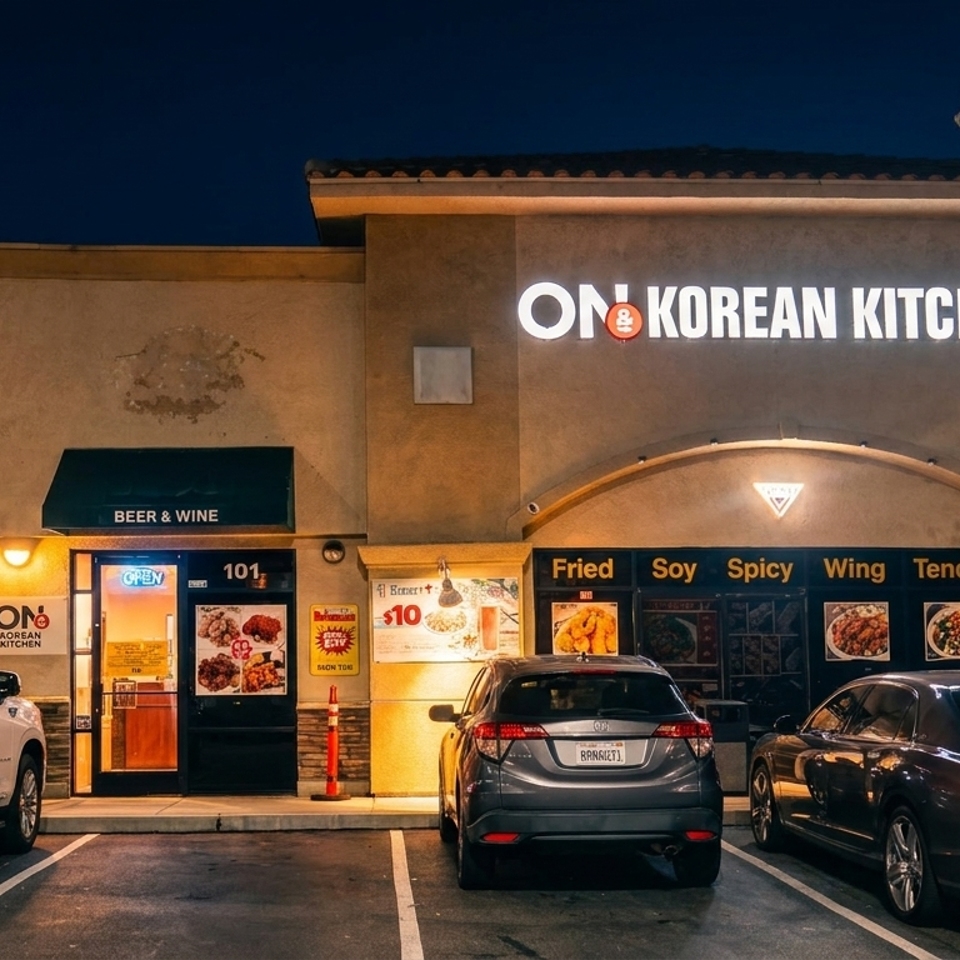 Korean restaurant storefront glowing at night, with illuminated signage, menu displays, autumn tree, and parked cars.
